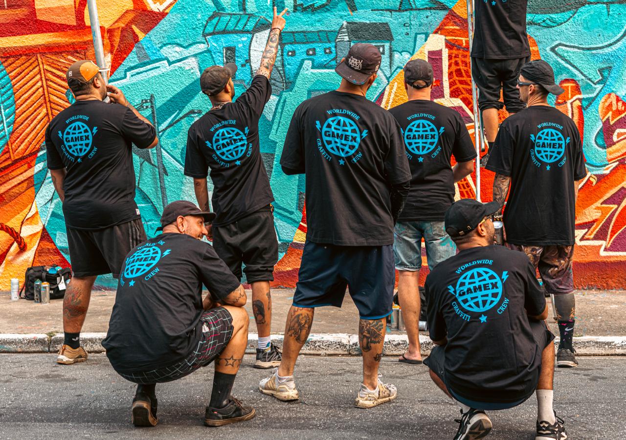 Integrantes de GAMEX con camisetas del crew frente a un mural